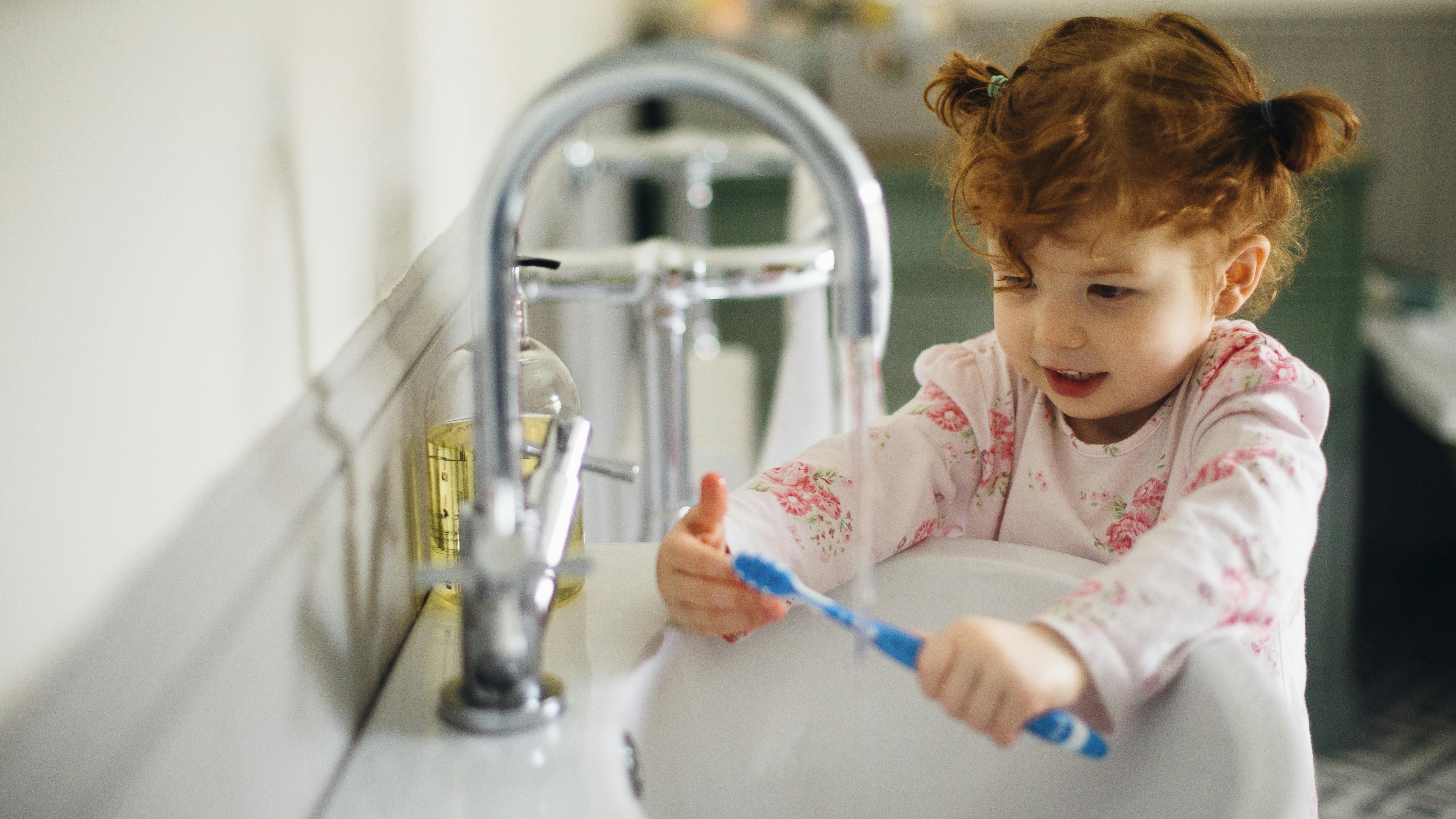 Child rinsing their toothbrush with water