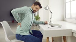 man sitting at a desk rubbing his sore back man sitting at a desk rubbing his sore back