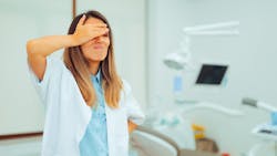 Frustrated professional stands in dental office with hand on forehead Frustrated professional stands in dental office with hand on forehead