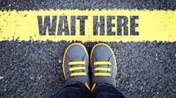 image of a person's feet standing at the edge of a yellow line that says 'wait here'