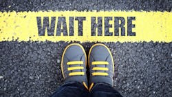 image of a person's feet standing at the edge of a yellow line that says 'wait here' image of a person's feet standing at the edge of a yellow line that says 'wait here'