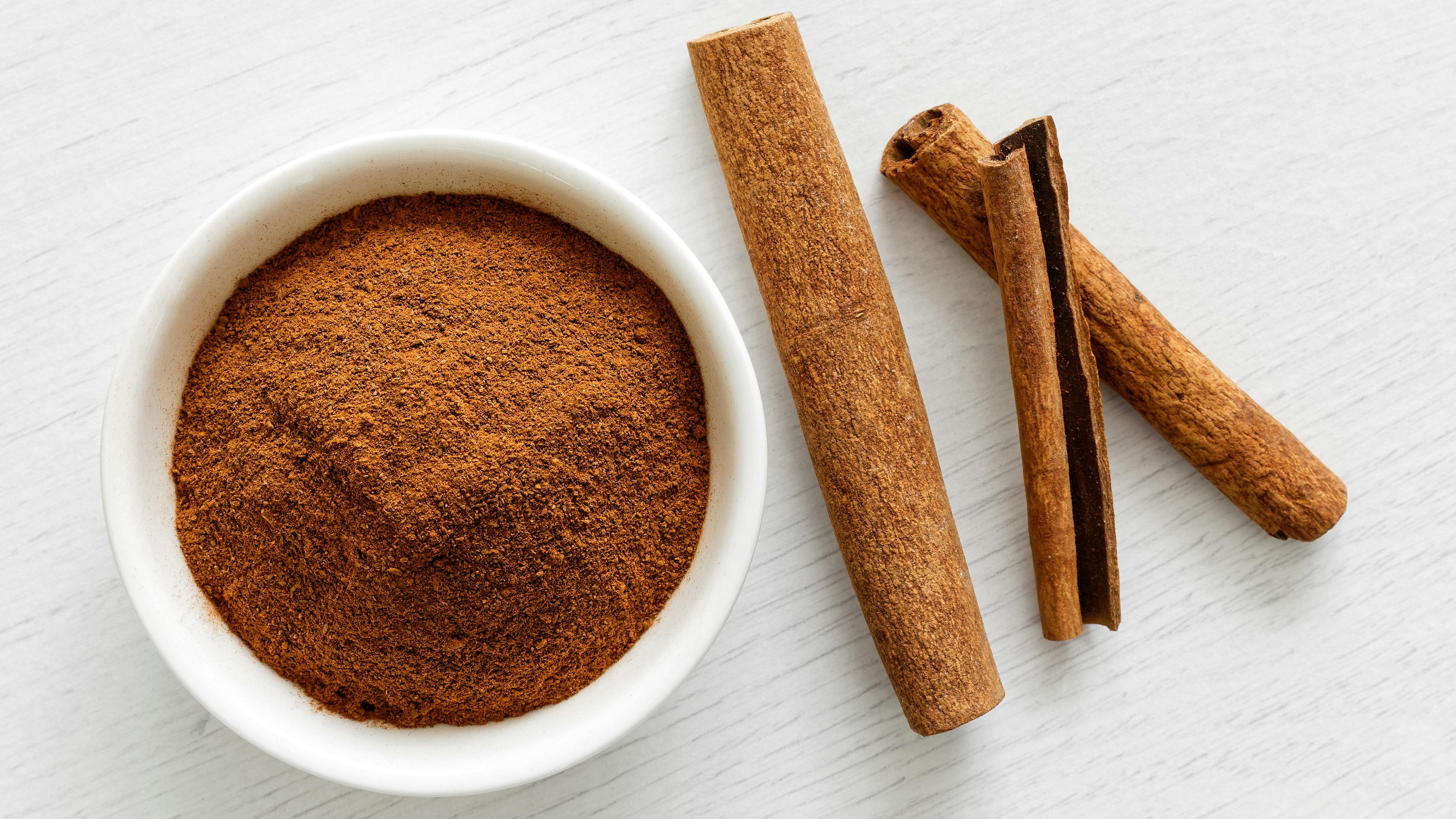 a bowl of ground cinnamon and some cinnamon sticks