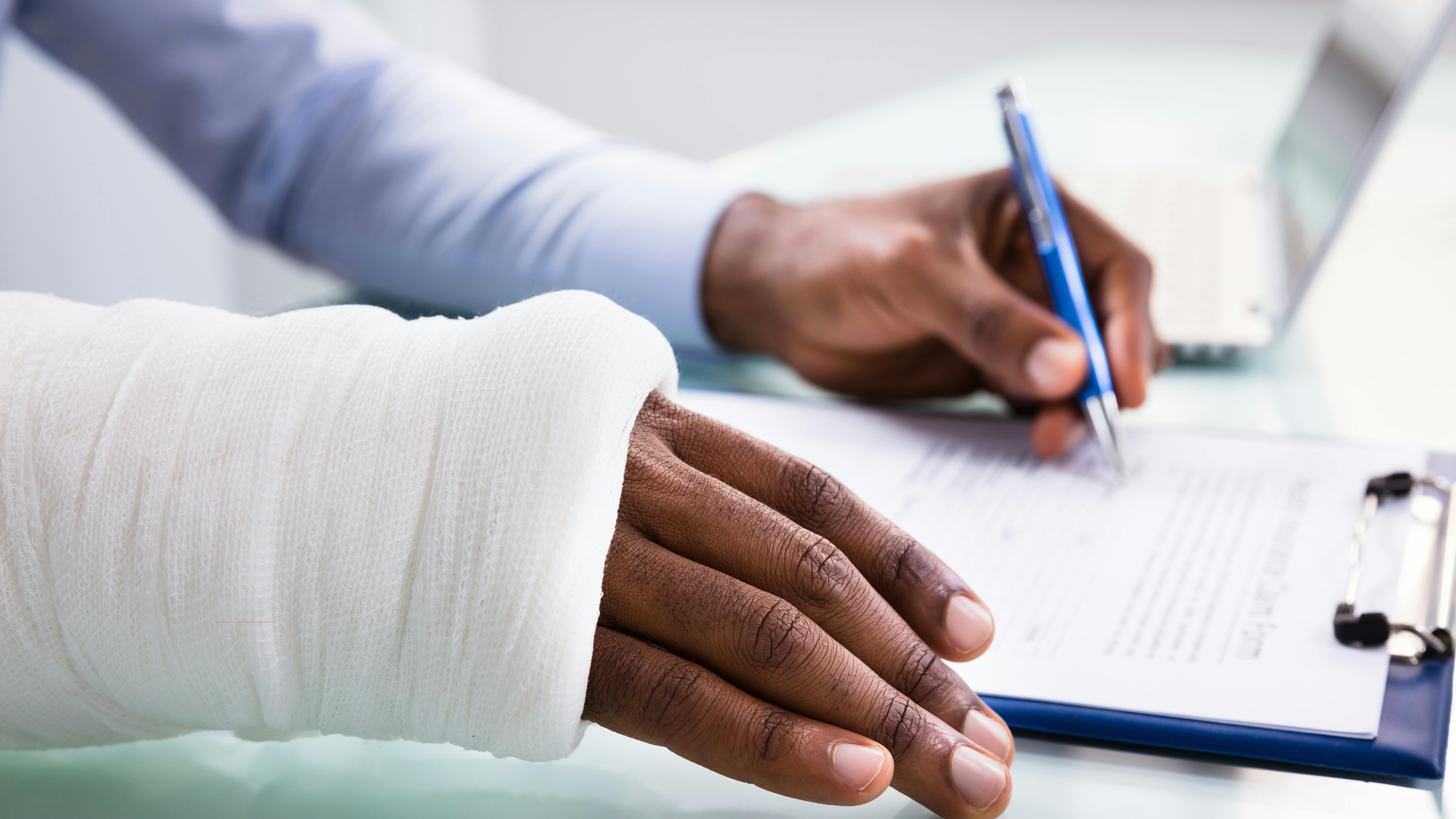 a man with a bandaged wrist filling out insurance paperwork