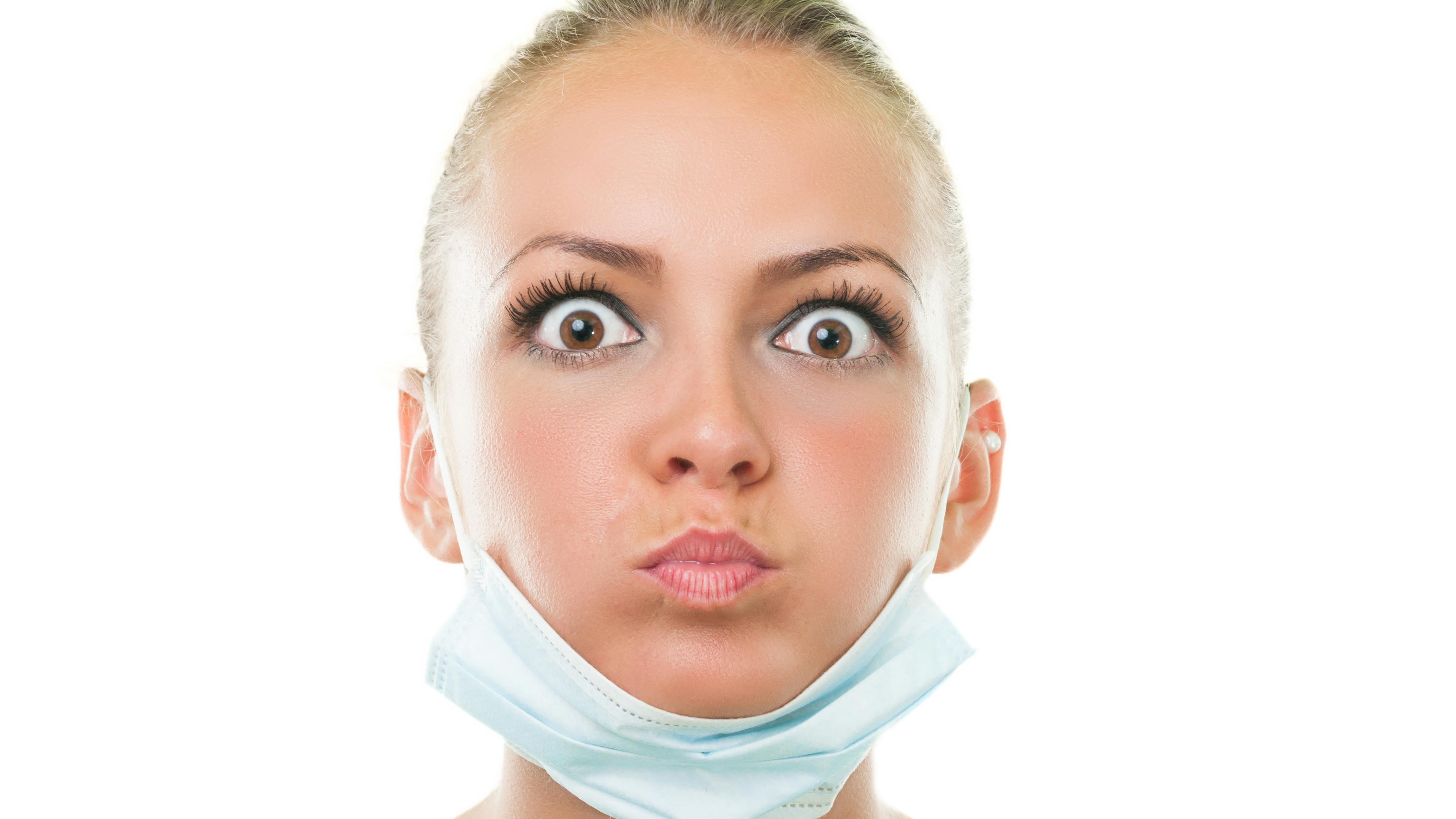 a startled-looking dental professional with a face mask down around her chin