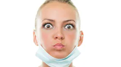 a startled-looking dental professional with a face mask down around her chin