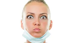 a startled-looking dental professional with a face mask down around her chin