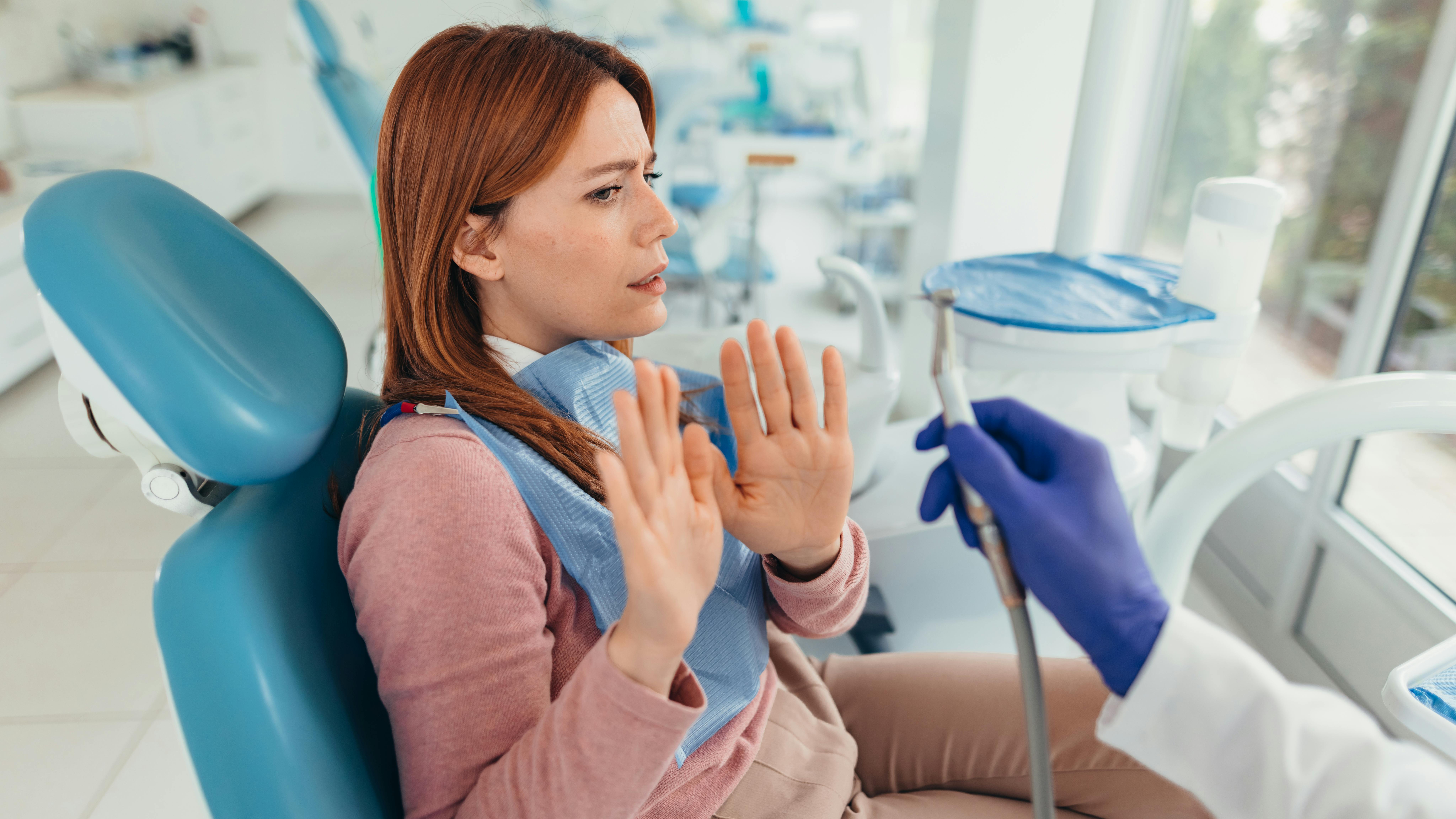 Young woman refusing dental treatment raising her hands in fear
